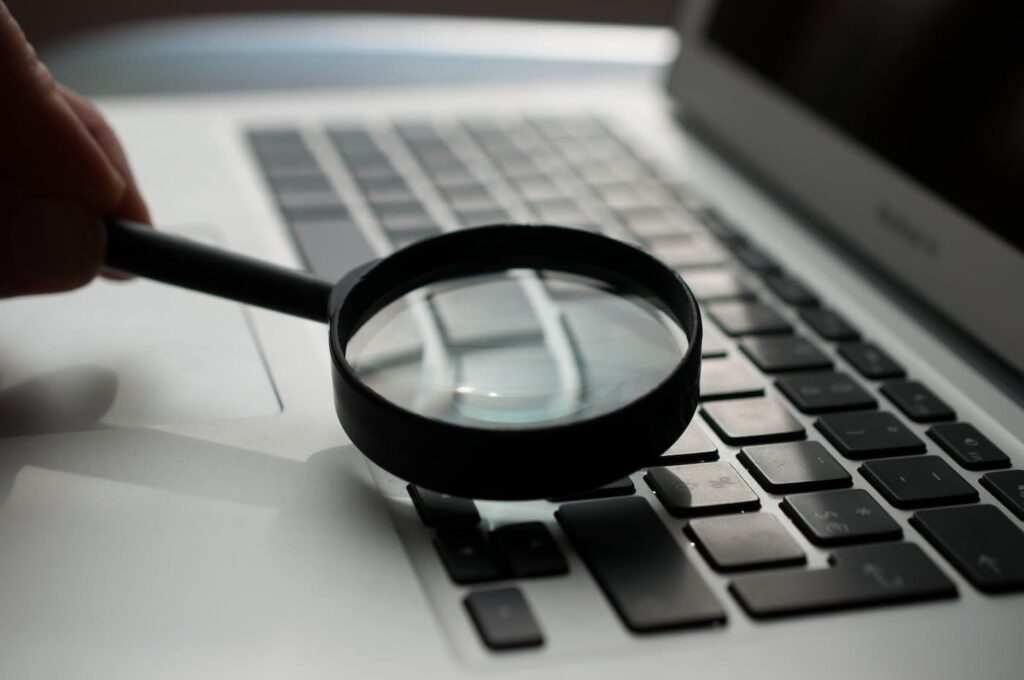 A magnifying glass hovering over a laptop keyboard, signifying the new screening requirements of SB 291