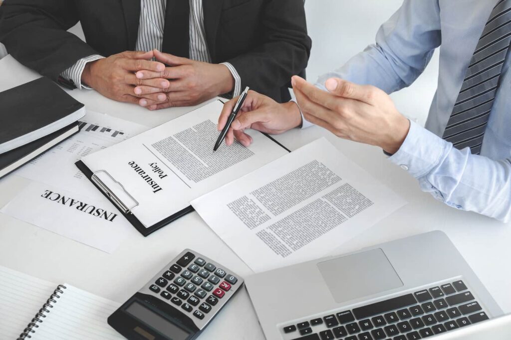 Two people in suits sitting at a desk with renters liability insurance paperwork spread in front of them