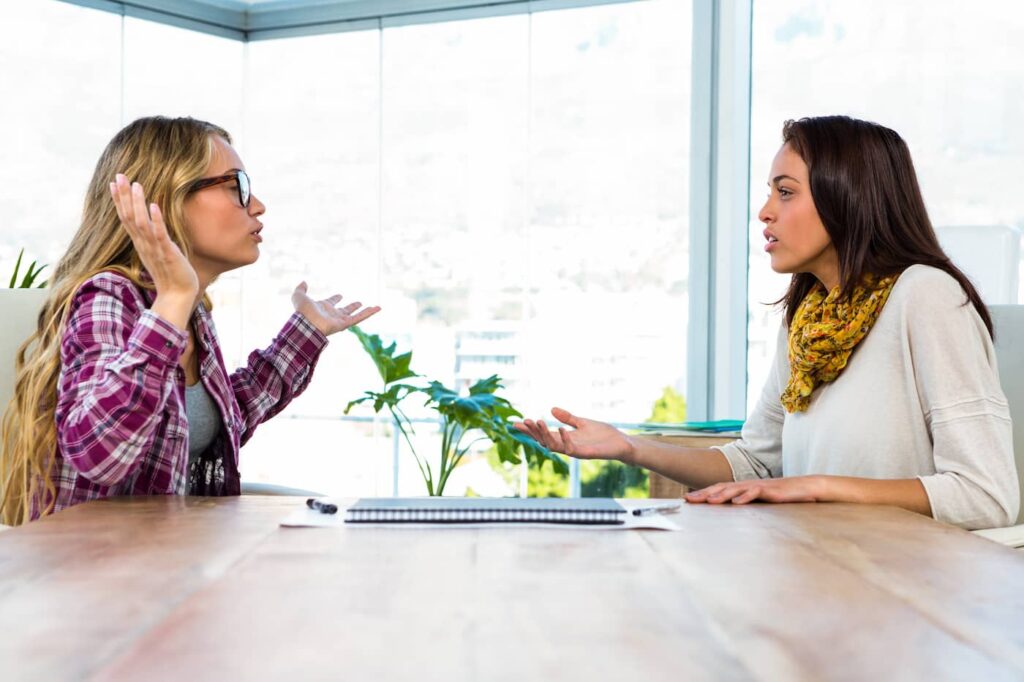 Two women sitting at a desk engaged in a dispute.