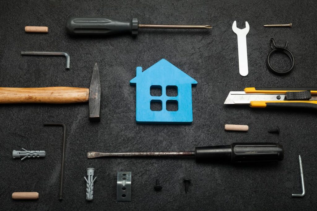 All the tools to tackle top maintenance issues laid out around a blue house on a table.