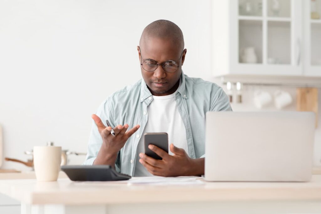 A landlord dealing with difficult tenants sits at his desk and gestures in frustration at his phone.