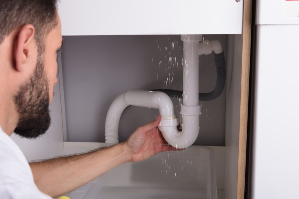 a man assessing a water leak underneath a sink.