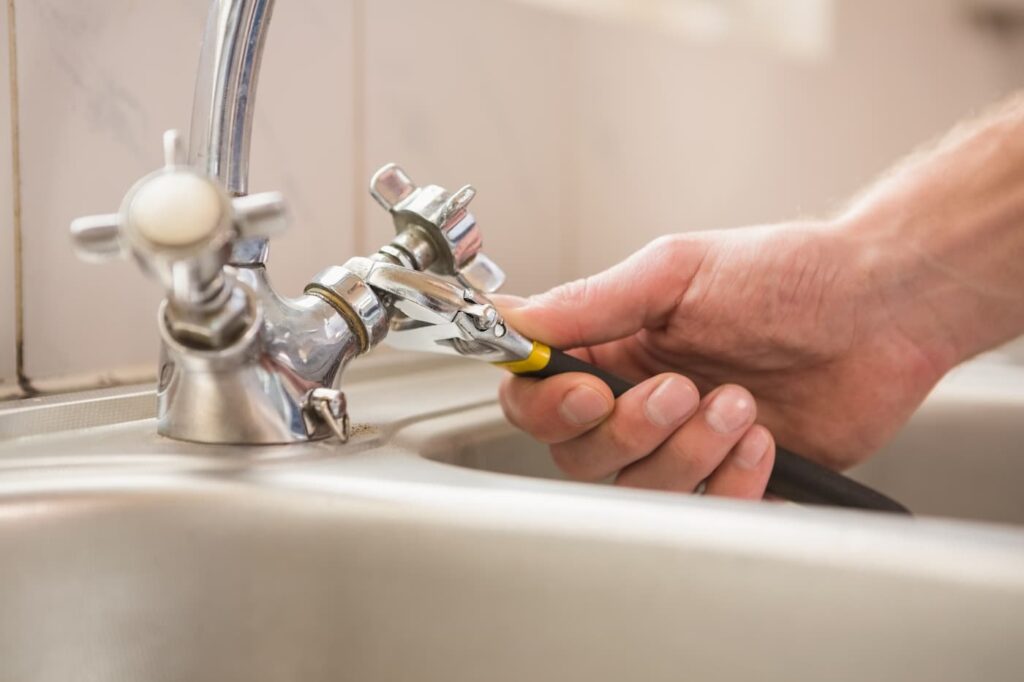 someone using a wrench to tighten a handle on a kitchen sink faucet fufilling tenant maintenance requests