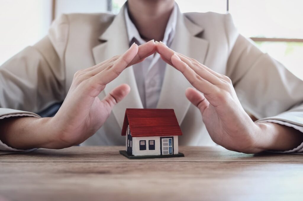 a person in a suit holding their hands over a small model home, illustrating the added security of renting a managed property.